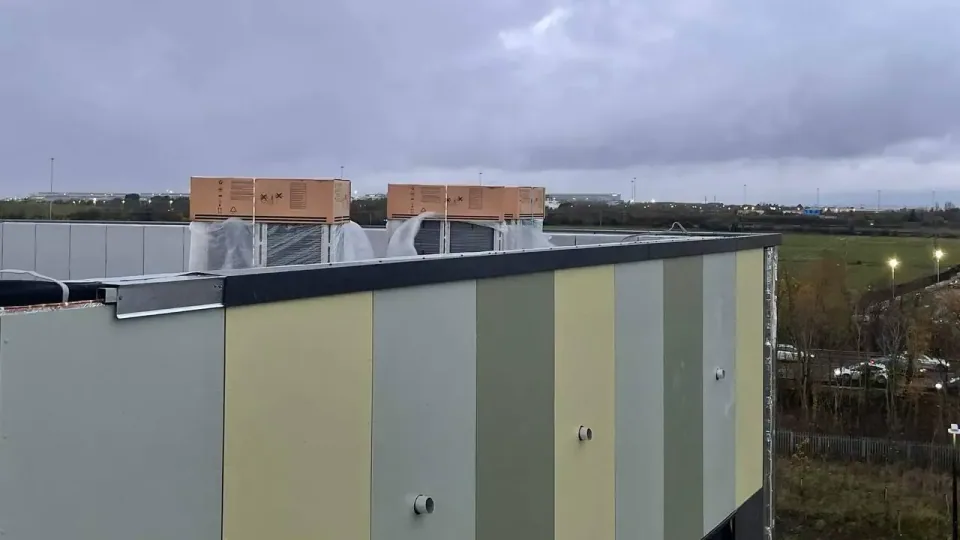 Dark aluminium parapet coping closing a green and grey architectural panel facade, rooftop plant units behind